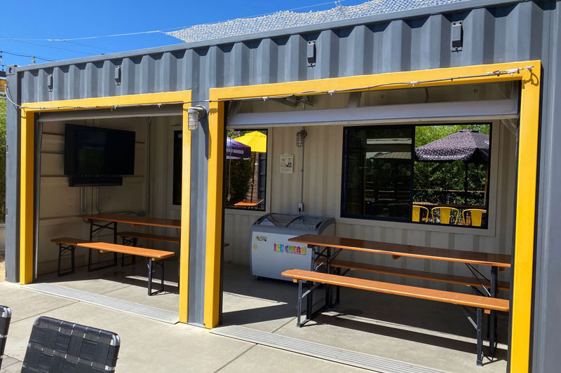 transformed metal shipping container for beer garden seating with tables and a tv