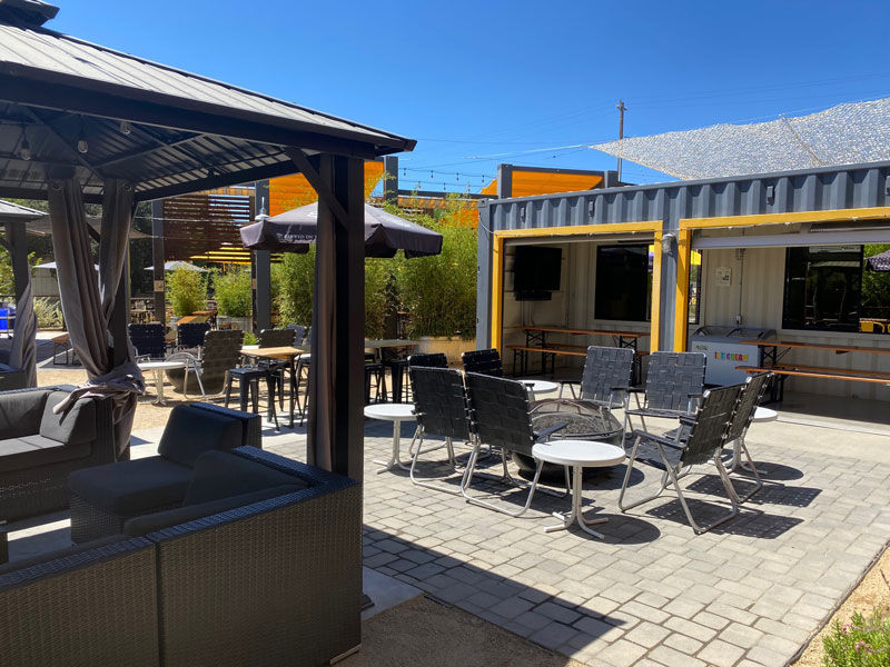 converted storage container in grey and yellow with beer garden tables a gazebo firepits and lawn chairs